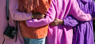 Four people in colourful fur coats holding each other's backs & standing in a line in support