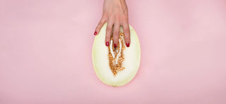 Hands with red fingernails against melon that resembles a vulva