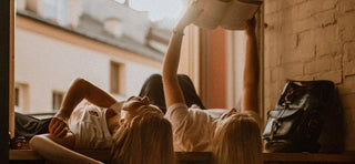 Two female friends lying on their back reading a book together