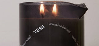 Close up of VUSH Massage Oil Candle in black candle holder with two flames burning