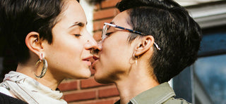 Two queer women with dark hair kissing with eyes closed
